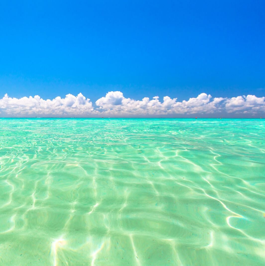 Clear turquoise ocean water under a bright blue sky with scattered white clouds on the horizon.